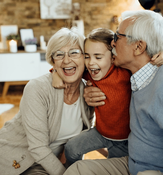 Imagem de avós abraçando e beijando uma neta